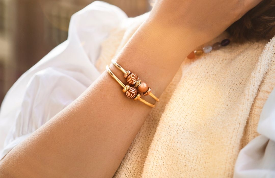 Close-up of two gold plated bangles styled with barrel beads and purple