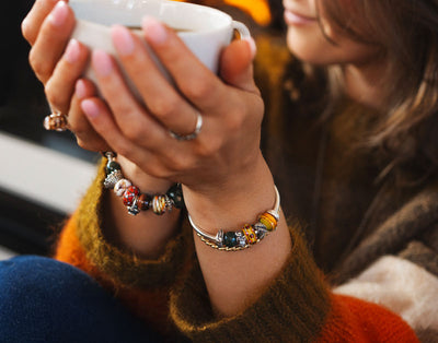 Trollbeads model reading a book by the fire, wearing the Autumn 2025 collection