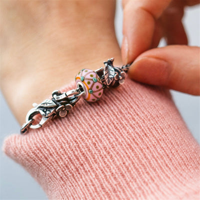 silver bracelet with beads and lock laying on wood on a grass field