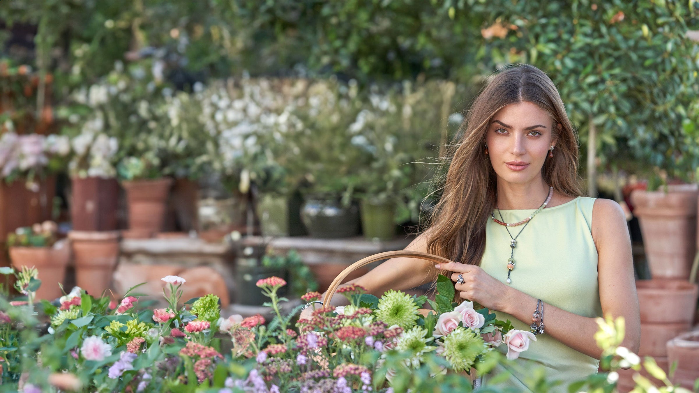 Model steht in einem Garten mit einem Korb voller Blumen und trägt Trollbeads-Schmuck